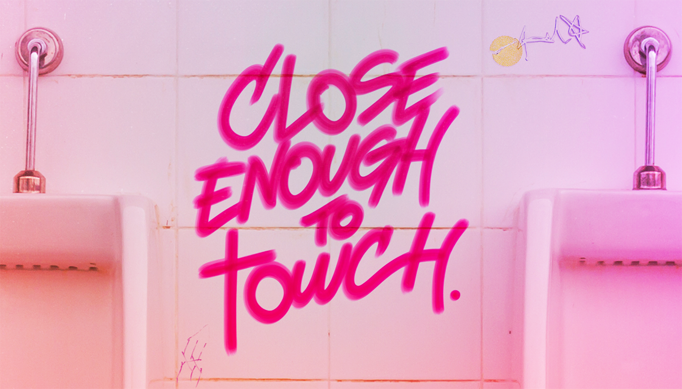 A graffiti title saying 'close enough to touch' in pink marker pen sits on the white tiles of a public toilet between two urinals