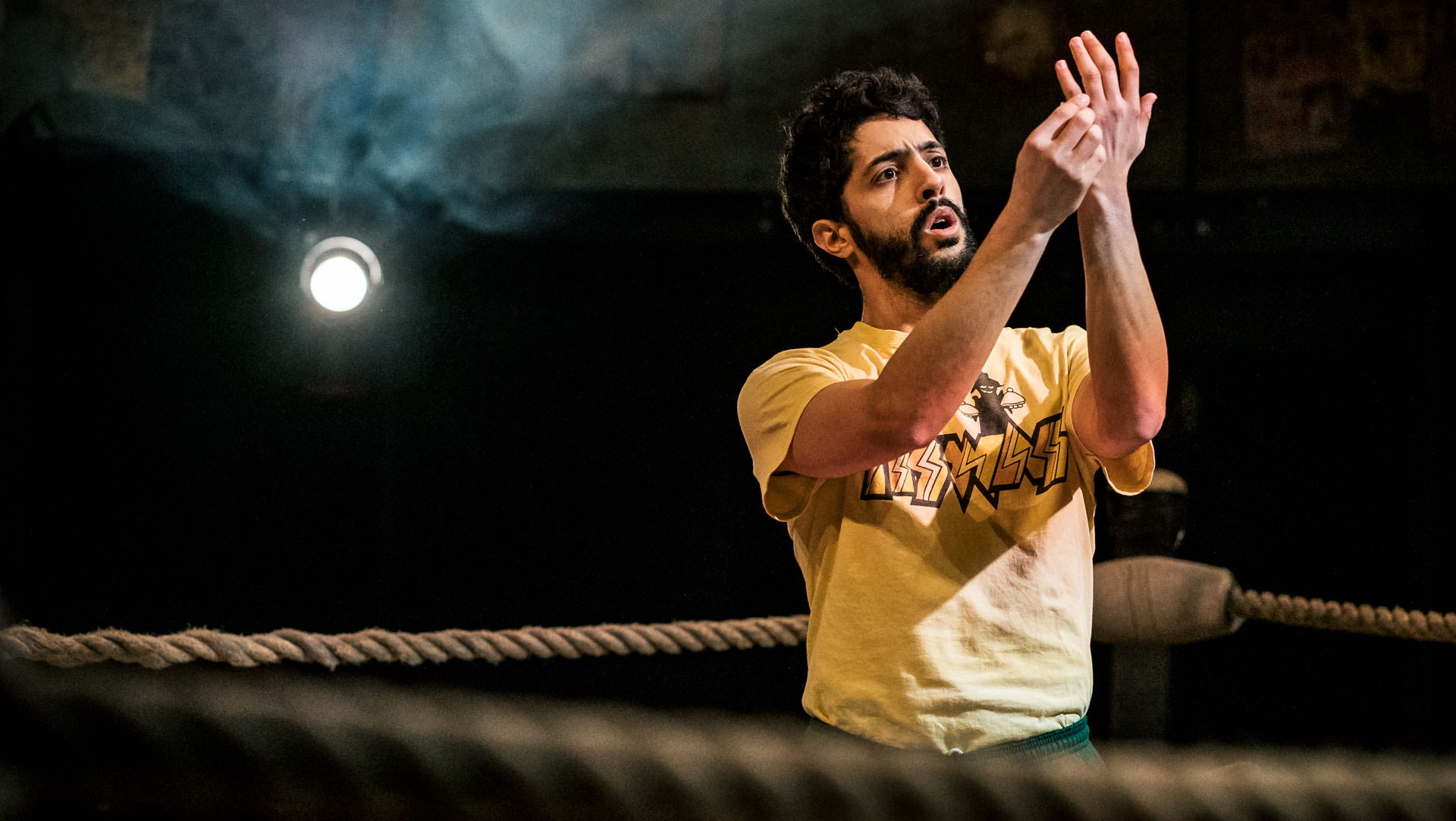 A wrestler in a t-shirt and bottoms studies his hands delicately in the ring