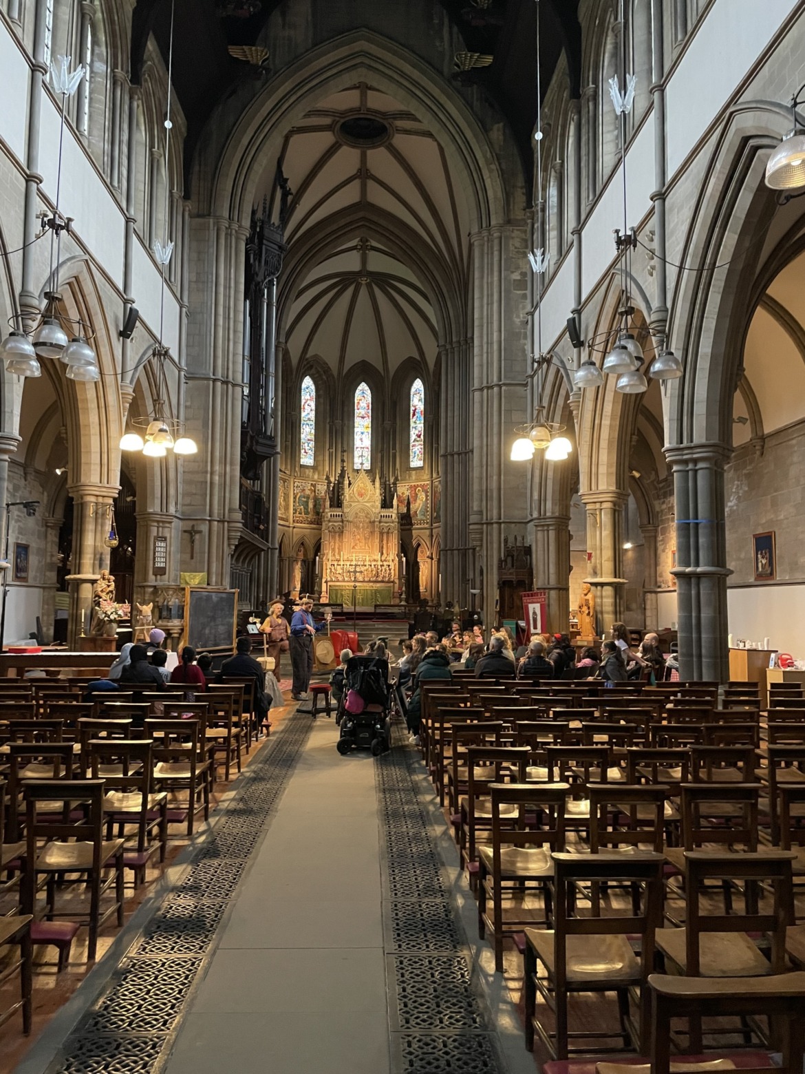 An audience watching a play in front of the stained glass windowns in an 18th century church