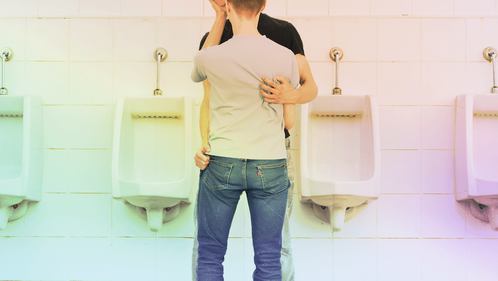 Two men in a passionate embrace in a urinals
