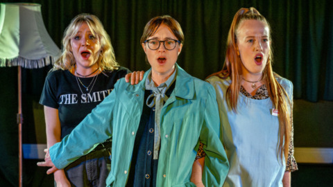 Three sisters holding onto each other and singing