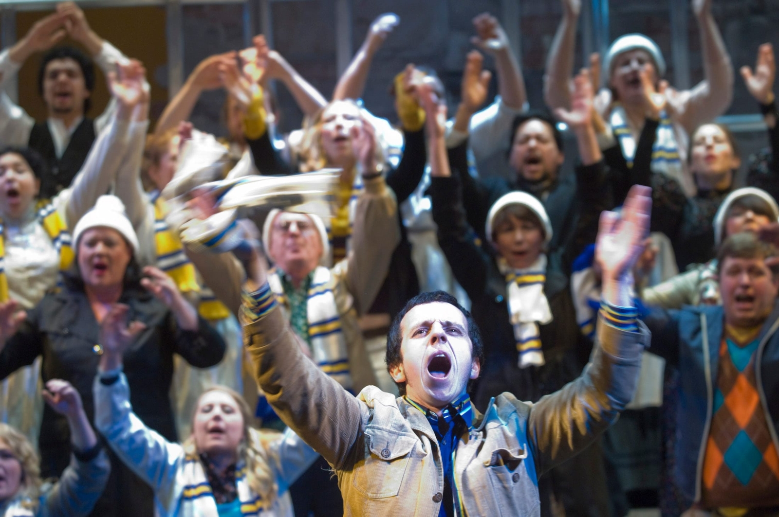 a crowd of Leeds United football fans singing with arms wide