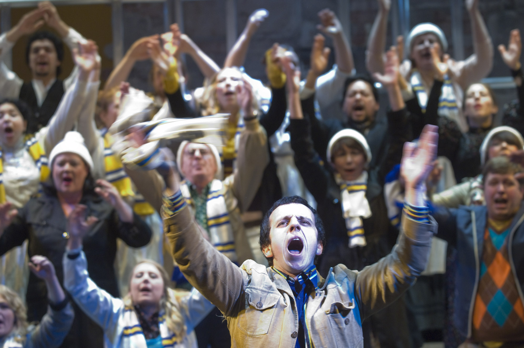 a crowd of Leeds United football fans singing with arms wide