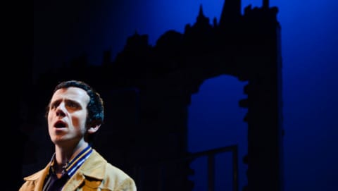 A man in seventies clothes singing with the Leeds skyline behind