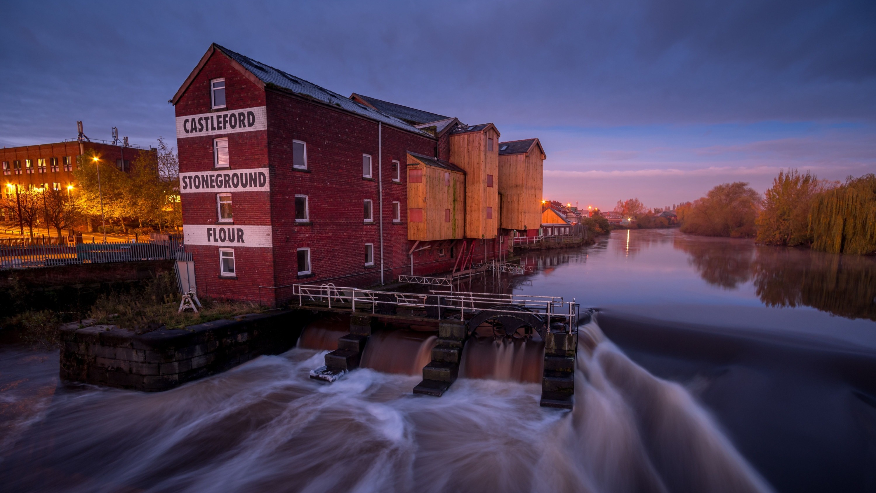 A Yorkhire flour mill on the side of the River Aire with the water gushing past.
