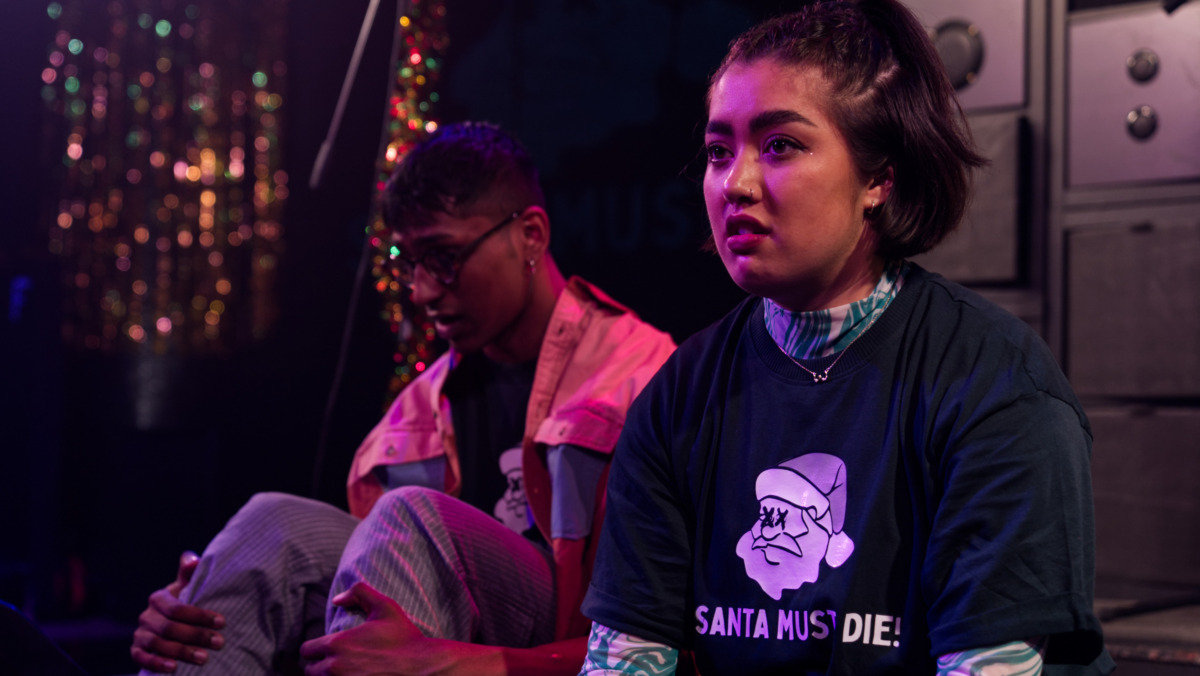 A man and woman sat despondently on a stage near instruments and a shimmer curtain