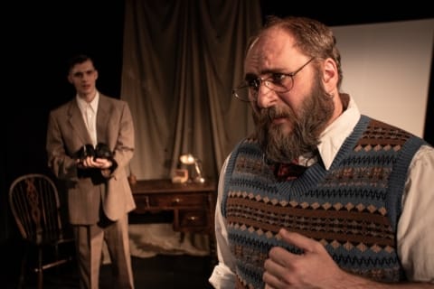 A young in a suit looks towards an older man looking troubled.