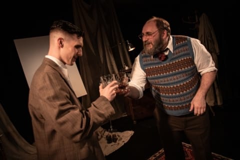 An older man in early 20th century dress passing a young man in WW1 British uniform a drink