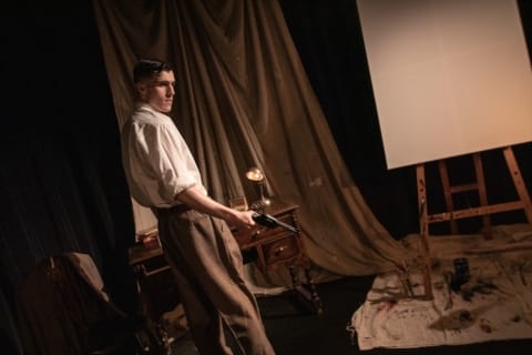 A young man with a gun stood in front of a blank canvas and easel