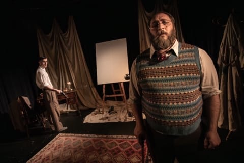 A young and older man in early 20th century dress in front of a blank canvas on an easel.