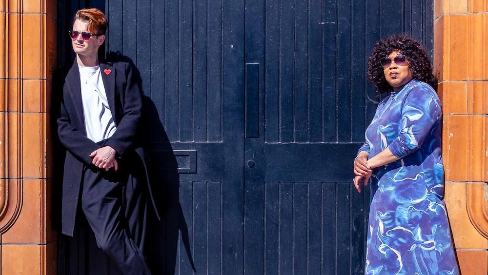 Cheryl and Alex casually leaning on walls in their shades