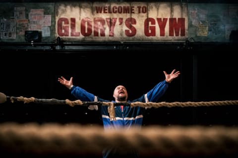 A wrestling coach with heads spread proudly under the sign of Glory's Gym