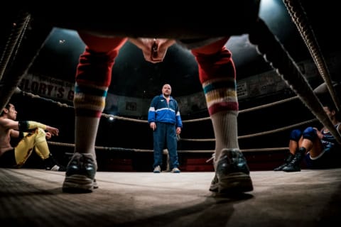 Looking through a wrestler's legs into a ring where a coach stands