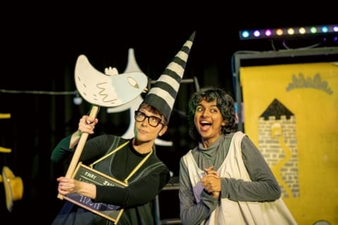 A girl in a pinafore looking gleeful and a dunce holding up a cardboard bird puppet