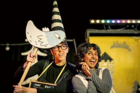 A girl in a pinafore looking gleeful and a dunce holding up a cardboard bird puppet