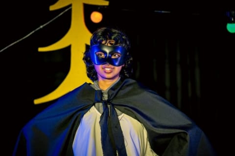 A girl in black mask and cape with arms spread