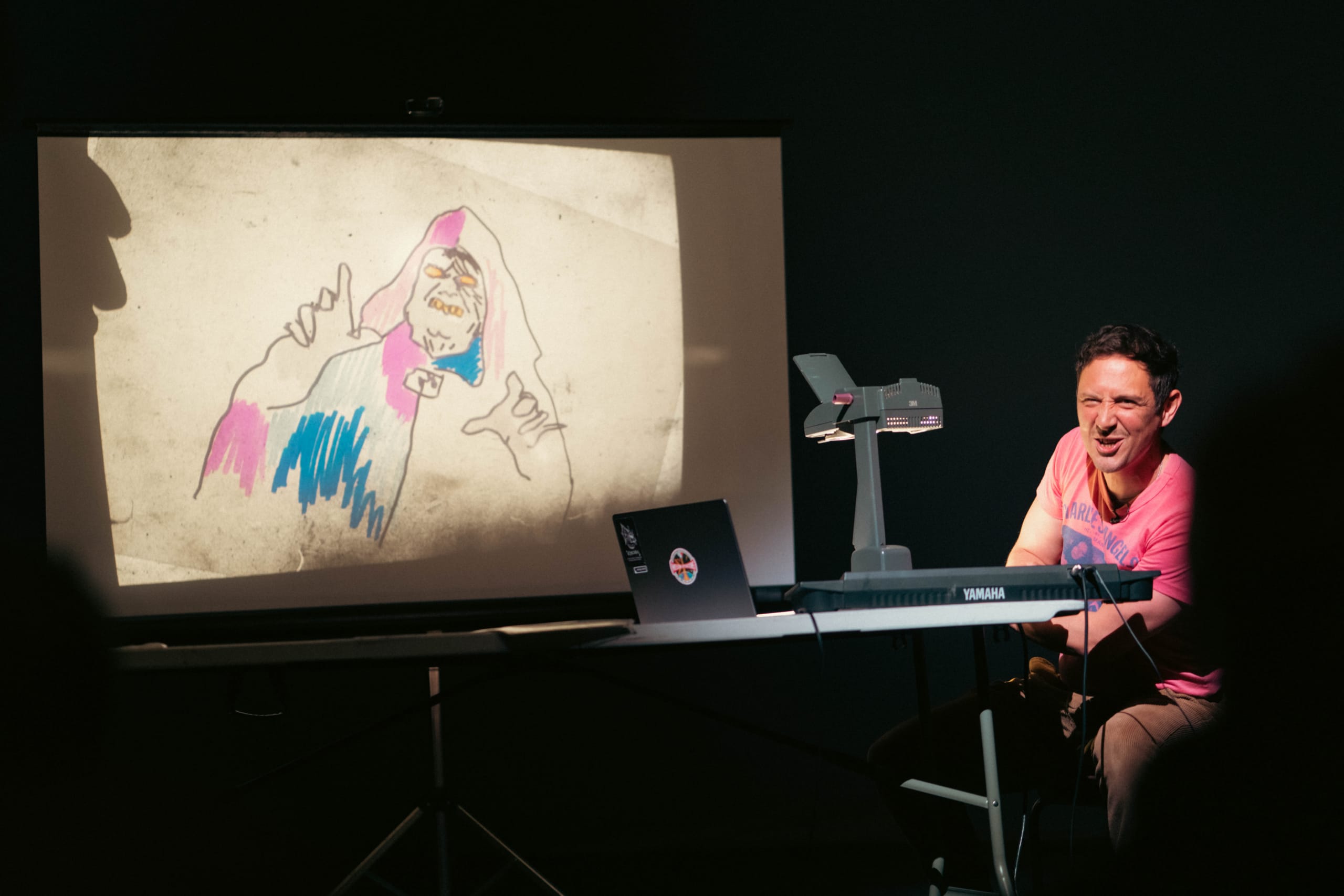Scott sat at his overhead projector with a drawn picture on the top, turning to the audience with delight