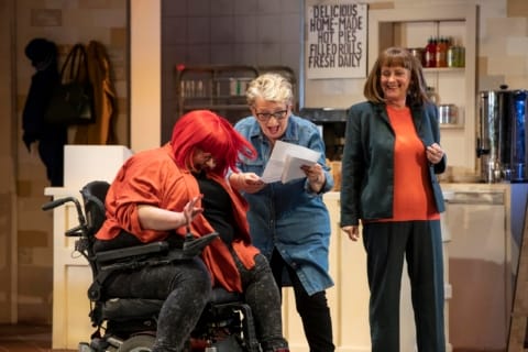 Three women laugh while looking at a piece of paper.