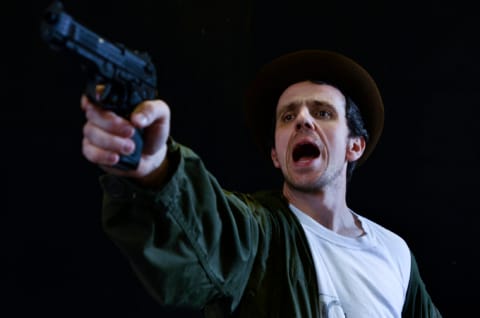 A man with a green jacket and brown hat, pointing a gun.