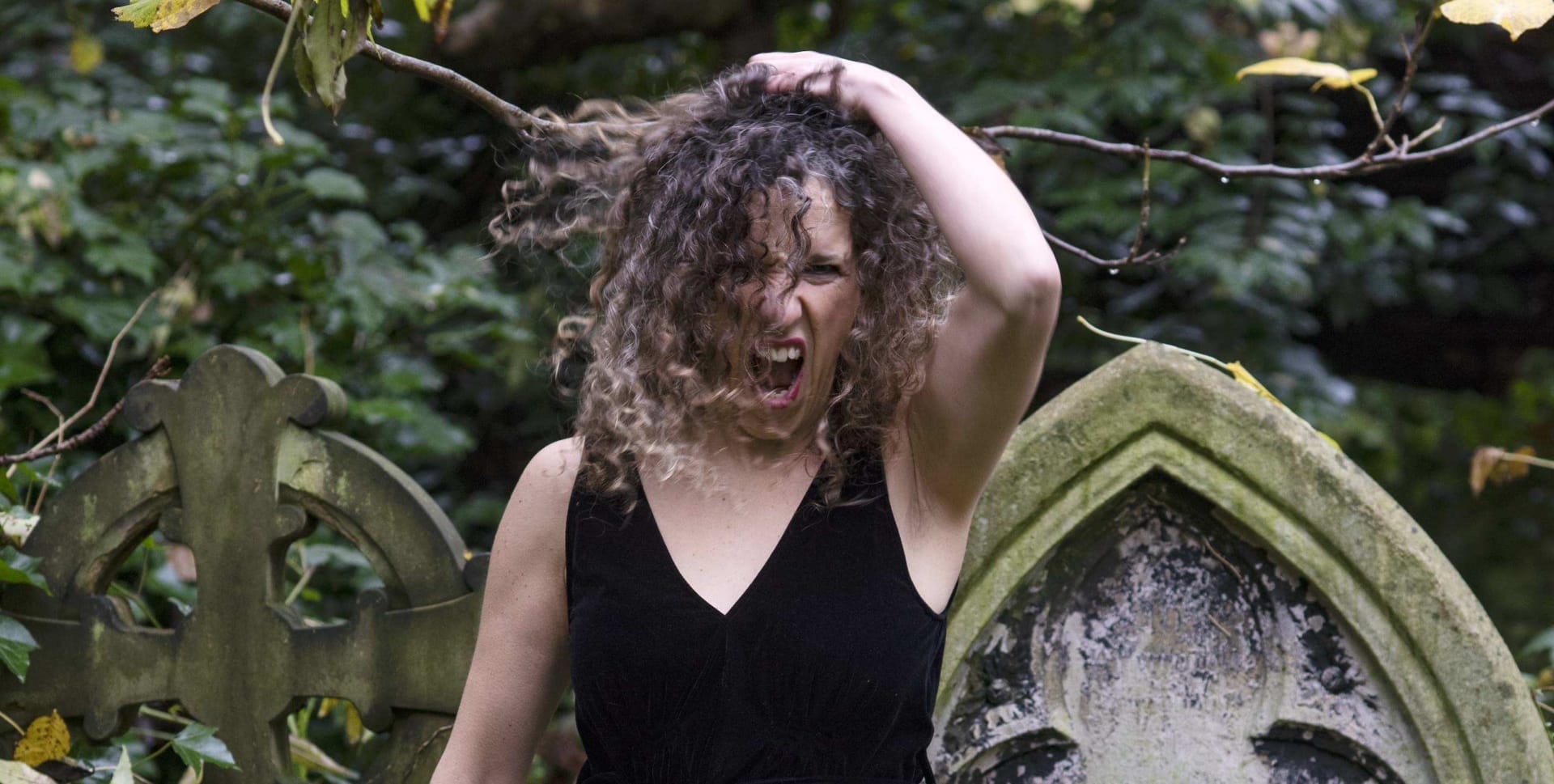 A woman in a graveyard holding her head and screaming
