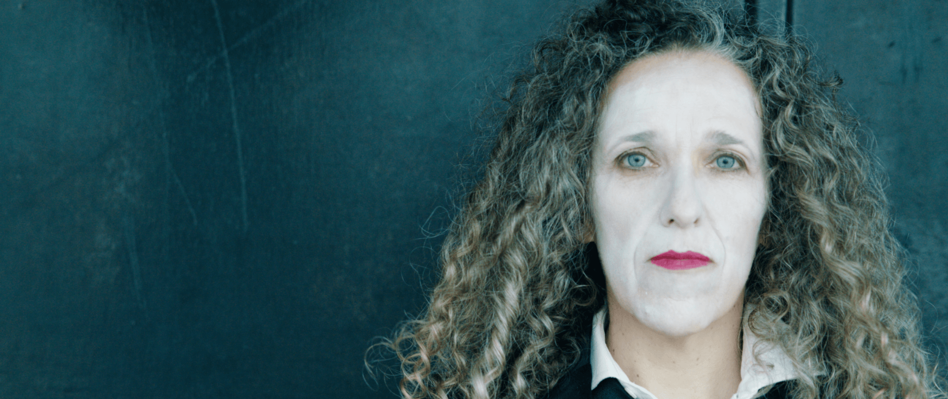 A woman in white face paint looking solemn
