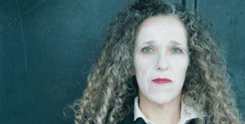 A woman in white face paint looking solemn