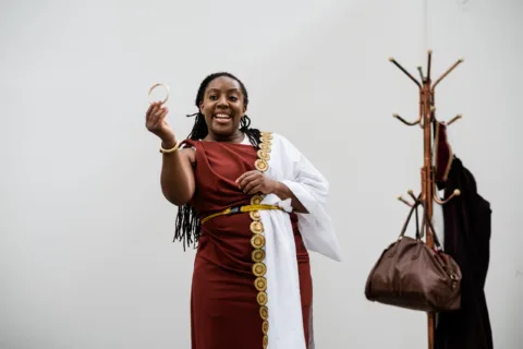 Alicia in ancient clothing holding up a coin