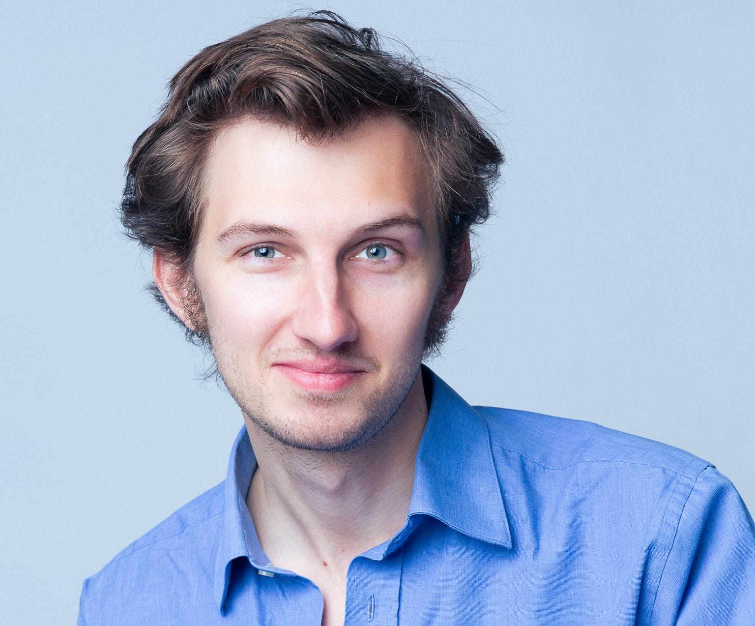 A young man in blue buttoned down shirt smiling to camera