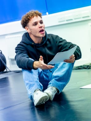 A young man sat on a rehearsal room floor with script in hand