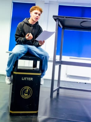 A young man sat on a public bin in a rehearsal room