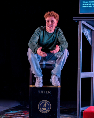 A young man sat on top of a public litter bin talking