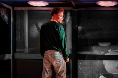 A young man at a urinal looking to his side as if suspicious