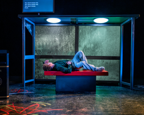 A young man laying on a bus shelter bench