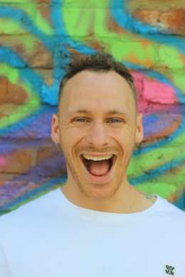 Chris stood against a spray painted wall with his mouth open smiling