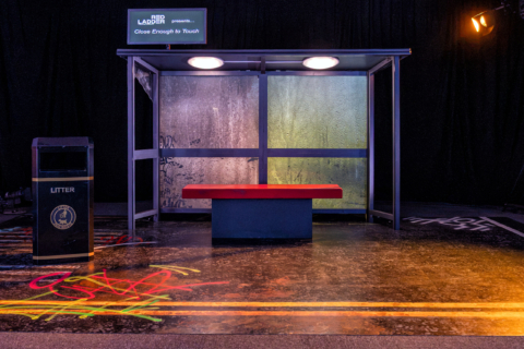 A bus shelter and bench on a set, lit by coloured stage lighting