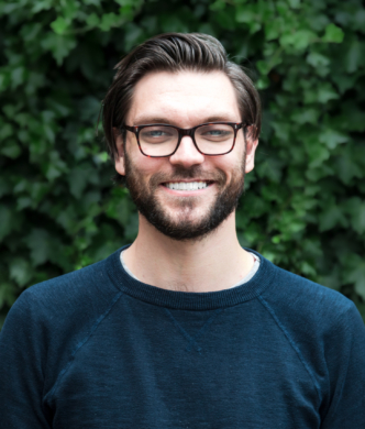 Adam stood smiling in front of a green hedge